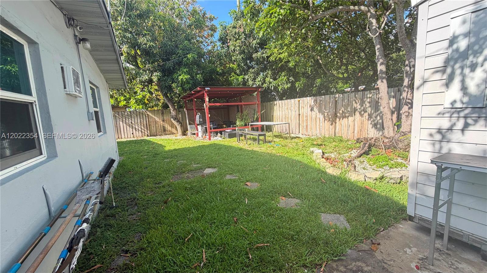 A grassy backyard features a red wooden pergola, a wooden fence, and mature trees — 3610 SW 39th Ave, West Park FL 33023, WEST PARK, FL