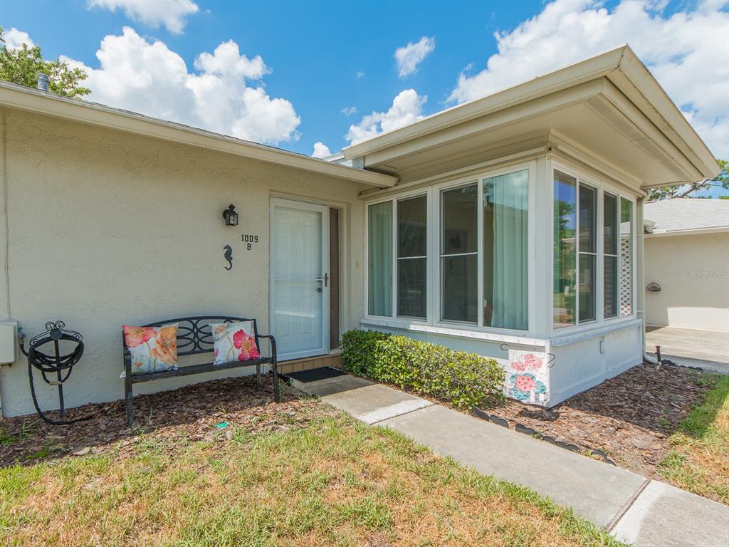 A beige house exterior features a white front door, a bench, and a sunroom — 1009 QUEEN ANNE DRIVE UNIT B, PALM HARBOR, FL