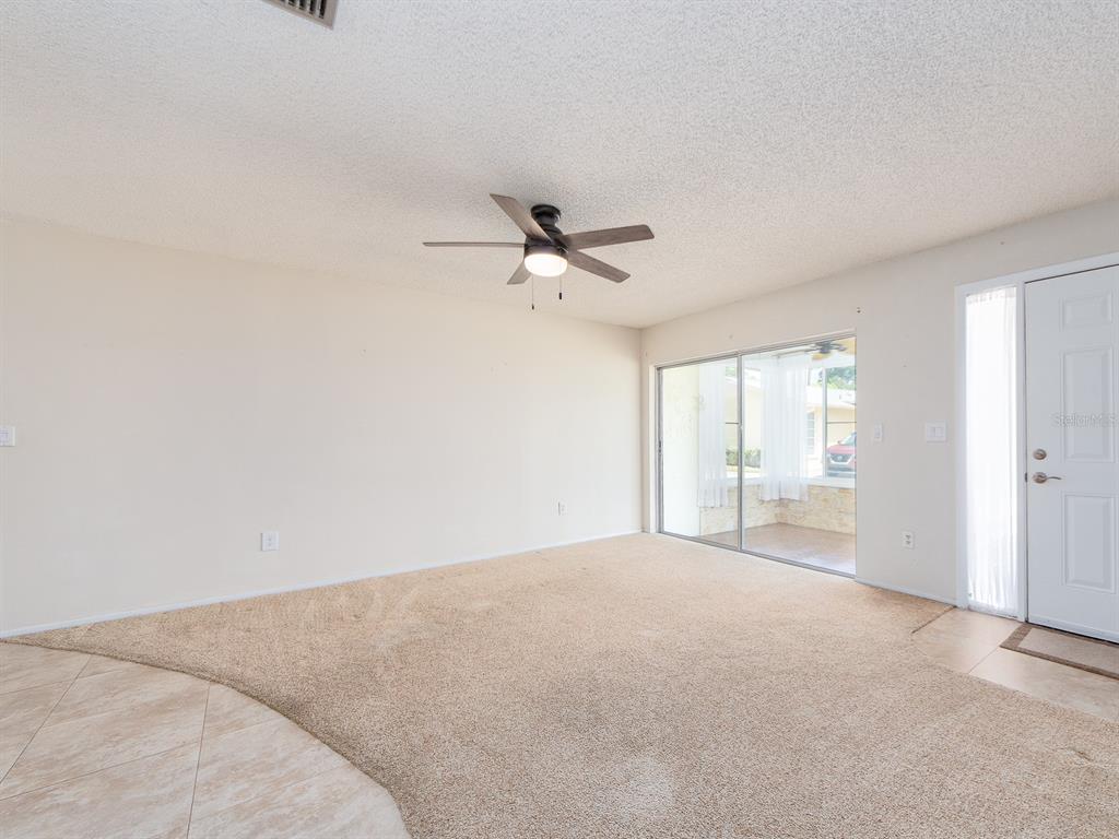 An empty living room features beige carpet, a ceiling fan, and a sliding glass door — 1009 QUEEN ANNE DRIVE UNIT B, PALM HARBOR, FL
