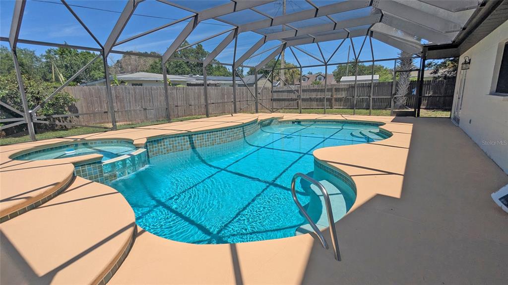 A screened-in swimming pool with an attached spa and a tan concrete deck — 1804 PONDEROSA LANE, TITUSVILLE, FL