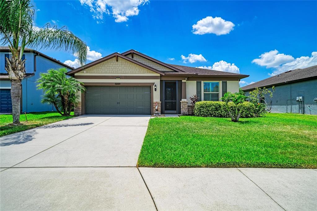 A single-story suburban house with a tan stucco exterior, a two-car garage, and a lawn — 11059 58TH STREET CIR E, PARRISH, FL