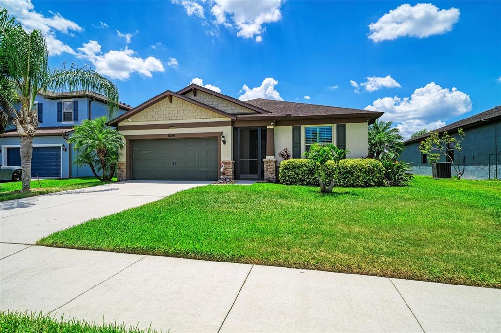 A single-story suburban house with a two-car garage, tan siding, and a green lawn — 11059 58TH STREET CIR E, PARRISH, FL