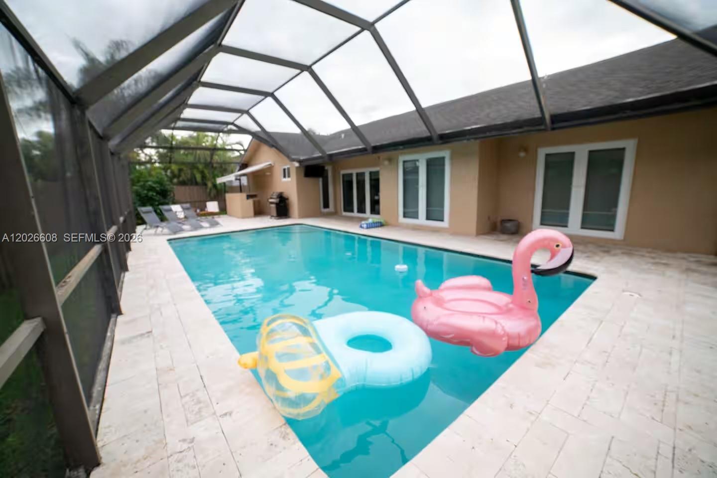 A screened-in swimming pool area features a patio with light-colored pavers and inflatable pool floats — 11931 SW 132nd Ave, Miami FL 33186, MIAMI, FL
