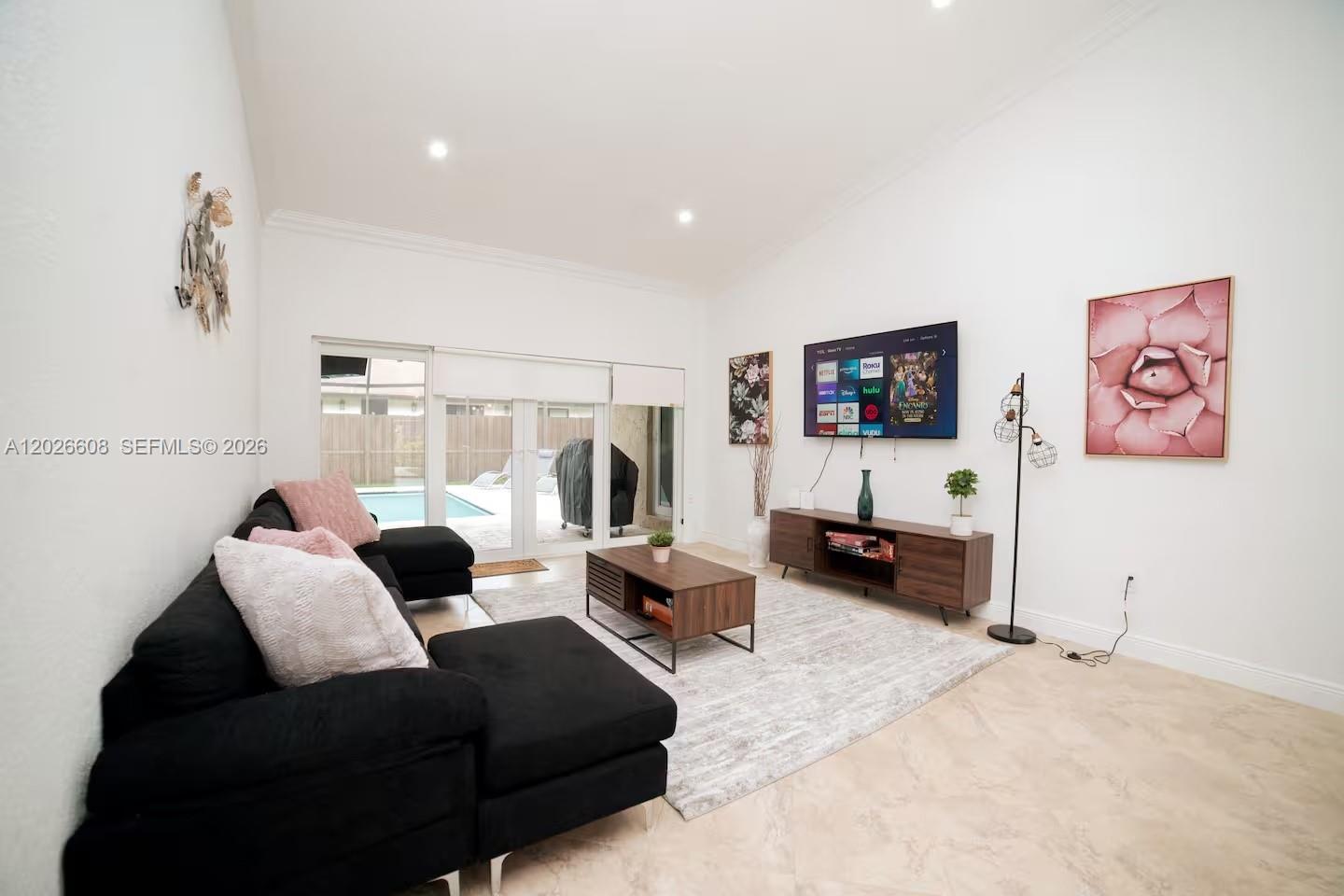 A living room features a black sectional sofa, a television, and sliding doors to a pool — 11931 SW 132nd Ave, Miami FL 33186, MIAMI, FL