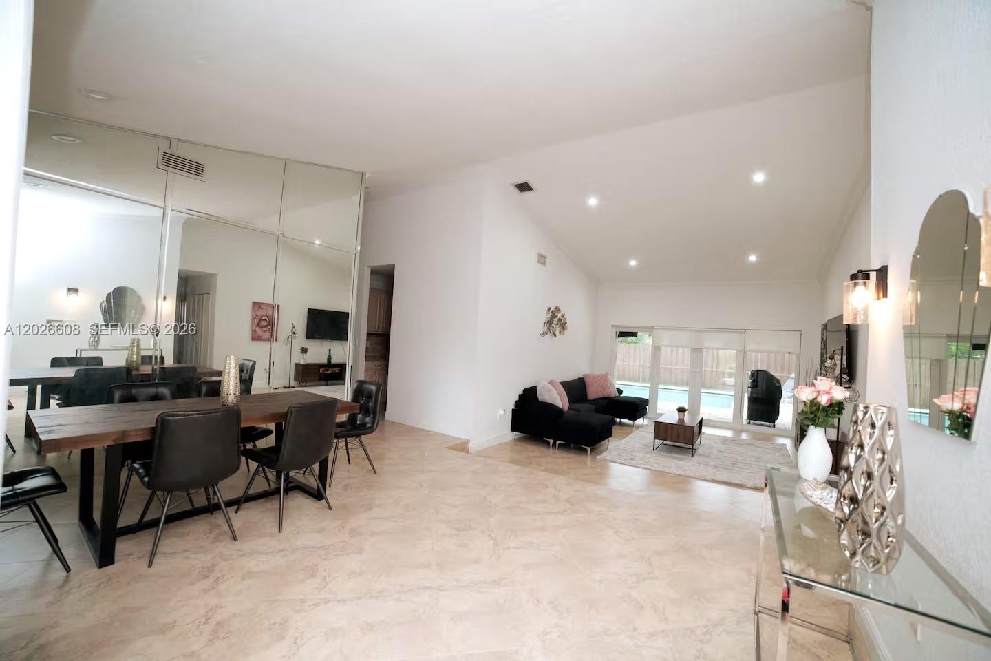 A living and dining area features tiled floors, mirrored walls, and a vaulted ceiling — 11931 SW 132nd Ave, Miami FL 33186, MIAMI, FL