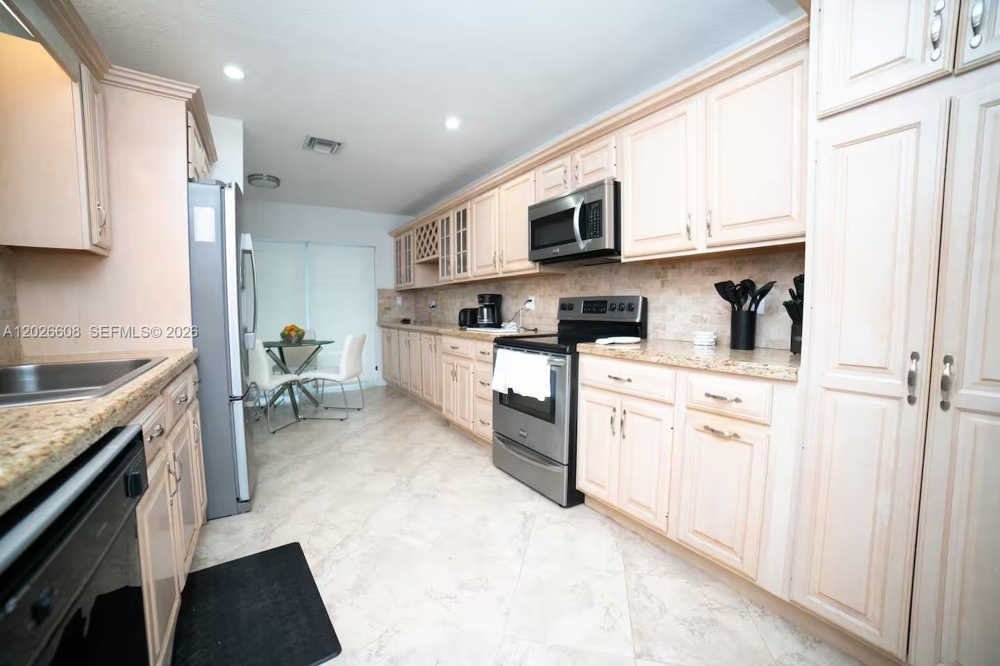 A kitchen features light wood cabinets, stainless steel appliances, and beige tile flooring — 11931 SW 132nd Ave, Miami FL 33186, MIAMI, FL