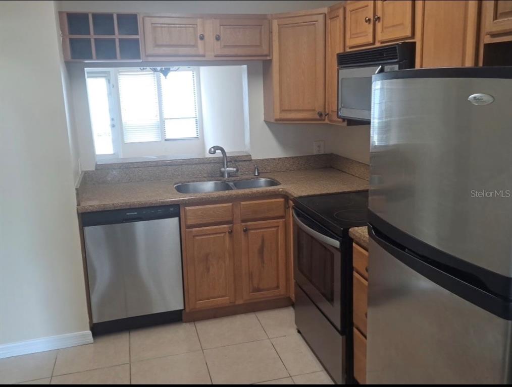 A kitchen features wood cabinets, stainless steel appliances, and a pass-through window above the sink — 2227 STONINGTON AVENUE UNIT 2227, ORLANDO, FL