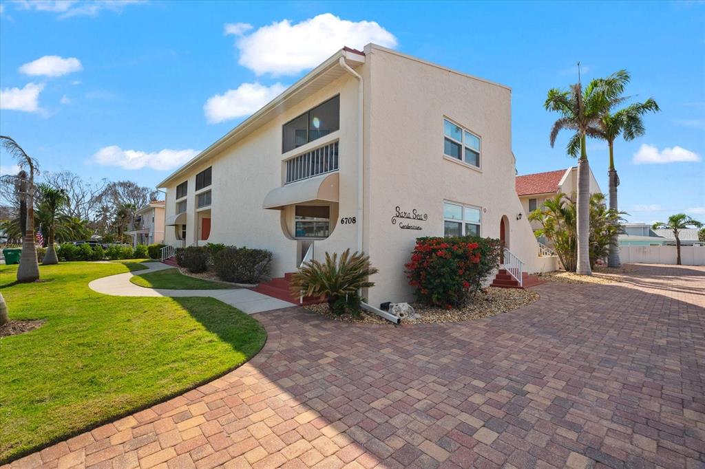 A two-story beige condominium building features a brick driveway, palm trees, and a grassy lawn — 6708 SARASEA CIRCLE UNIT 202, SARASOTA, FL