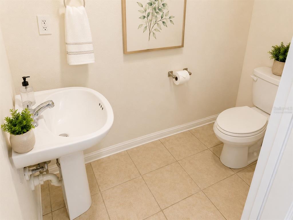 A small bathroom features a pedestal sink, a toilet, and beige tile flooring — 5001 SUNRIDGE PALMS DRIVE, TAMPA, FL
