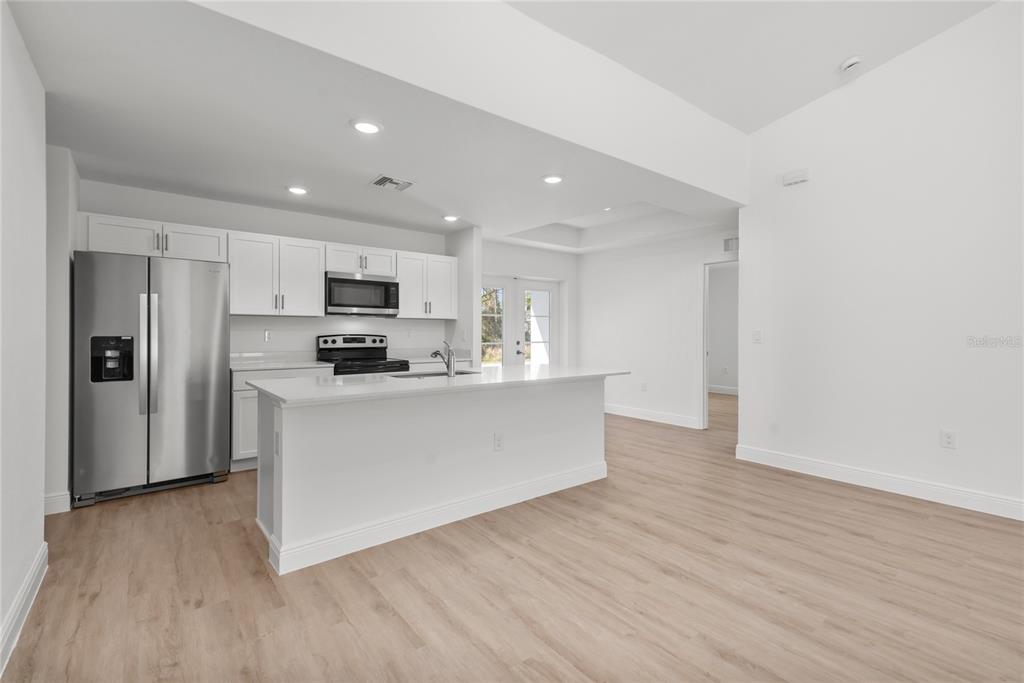 A modern kitchen features white cabinetry, stainless steel appliances, and a central island with countertops — 107 BLUE ROAD, ROTONDA WEST, FL