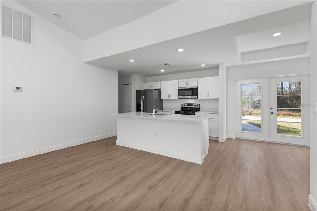 A modern kitchen features white cabinetry, a central island, and light wood-look flooring — 107 BLUE ROAD, ROTONDA WEST, FL