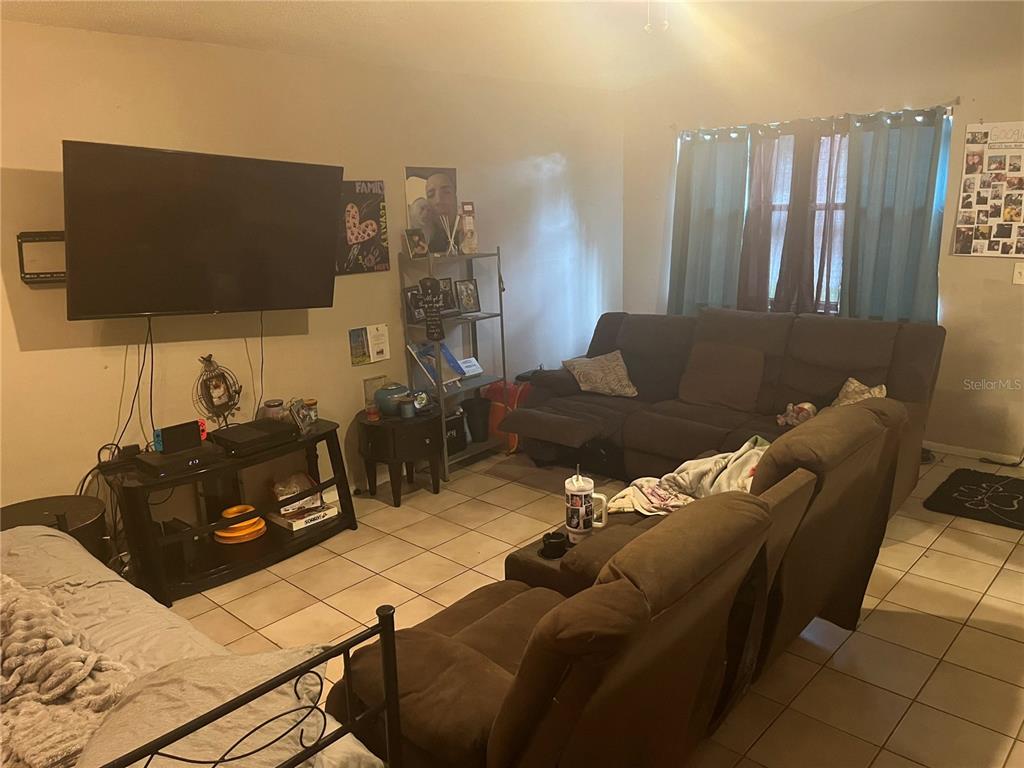 A living room features a large television, brown sectional sofa, and light-colored tile flooring — 9463 ARBOL COURT, LARGO, FL