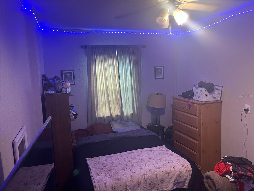 A bedroom features a bed, a wooden dresser, a window with curtains, and blue LED lighting — 9463 ARBOL COURT, LARGO, FL