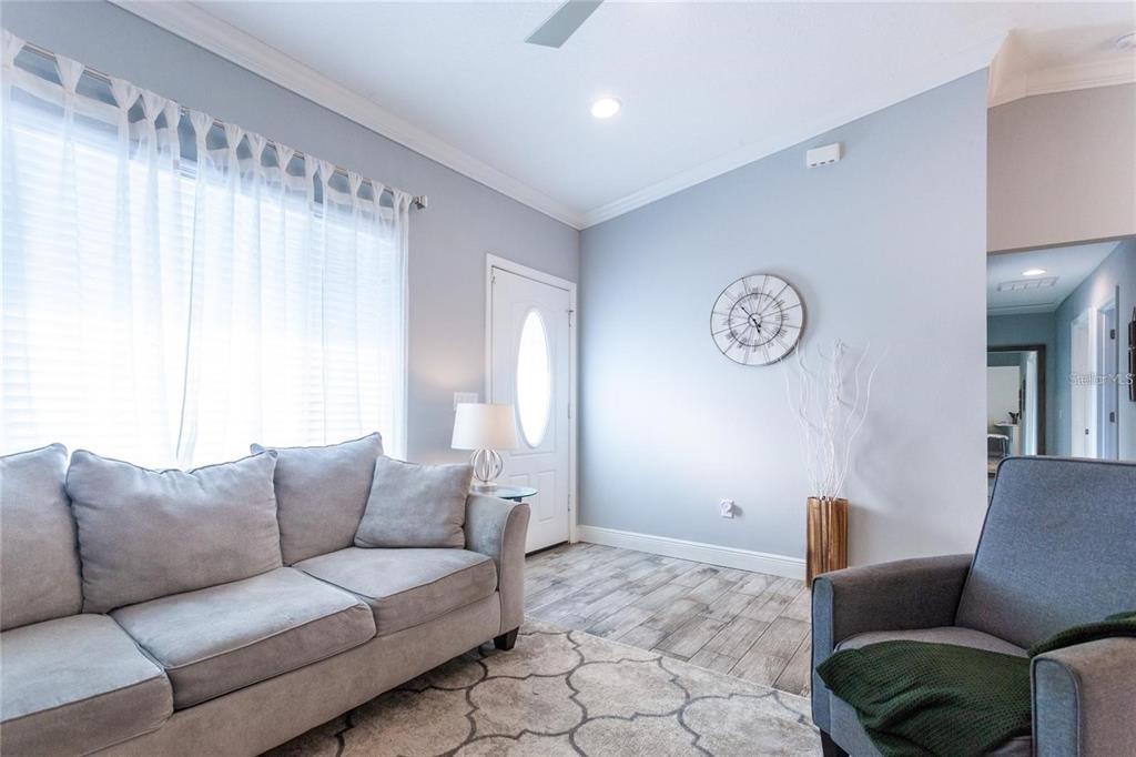 A living room features light blue walls, wood-look tile flooring, a gray sofa, and armchair — 691 E COUNTRY CLUB DRIVE, WILLISTON, FL