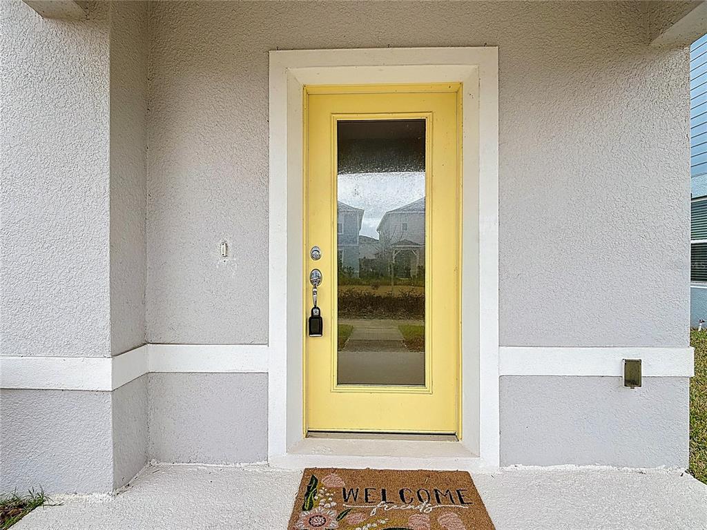 A yellow front door with a glass panel is centered on a grey stucco wall — 1823 SUMMER SERENITY DRIVE, KISSIMMEE, FL