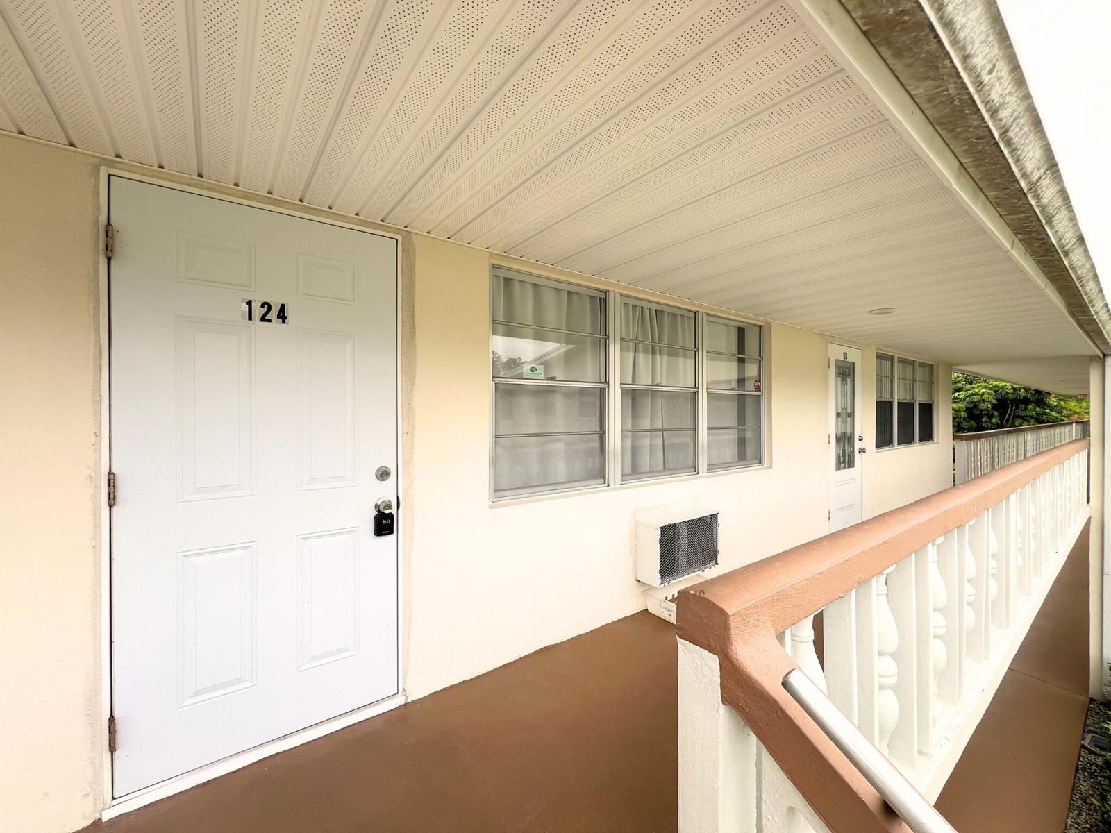 An exterior walkway leads to a white door numbered 124 with a window and AC unit — 124 E Andover E # 124, West Palm Beach FL 33417, WEST PALM BEACH, FL