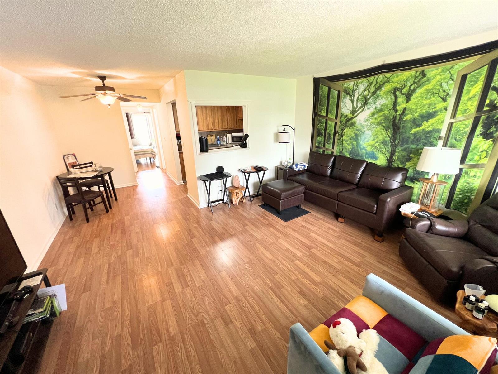 A living room with wood-look flooring, a brown leather sofa, and a forest-themed wall mural — 124 E Andover E # 124, West Palm Beach FL 33417, WEST PALM BEACH, FL