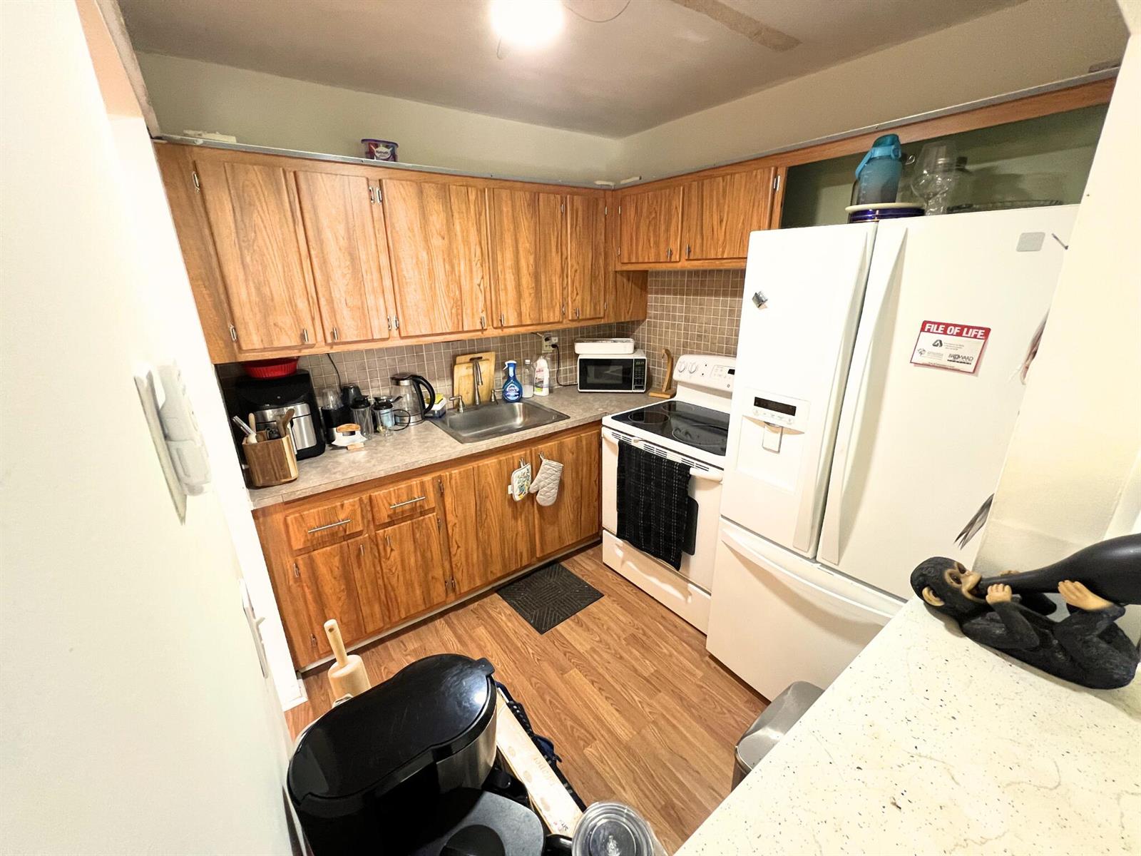 A galley kitchen features wood cabinets, white appliances, a tiled backsplash, and wood-look flooring — 124 E Andover E # 124, West Palm Beach FL 33417, WEST PALM BEACH, FL