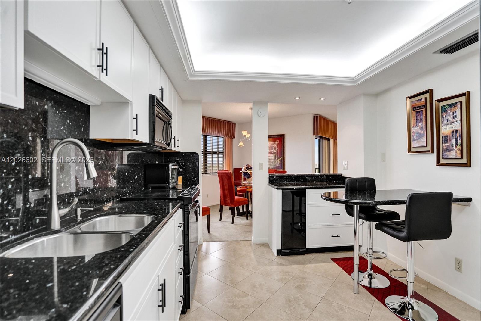 A kitchen with white cabinets, black granite countertops, and a small breakfast bar with stools — 501 N Riverside Dr, Pompano Beach FL 33062, POMPANO BEACH, FL