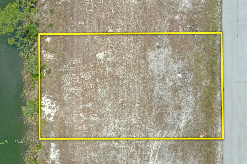 An aerial view shows a rectangular, undeveloped lot situated between a road and a canal — 2831 NE 5TH PLACE, CAPE CORAL, FL