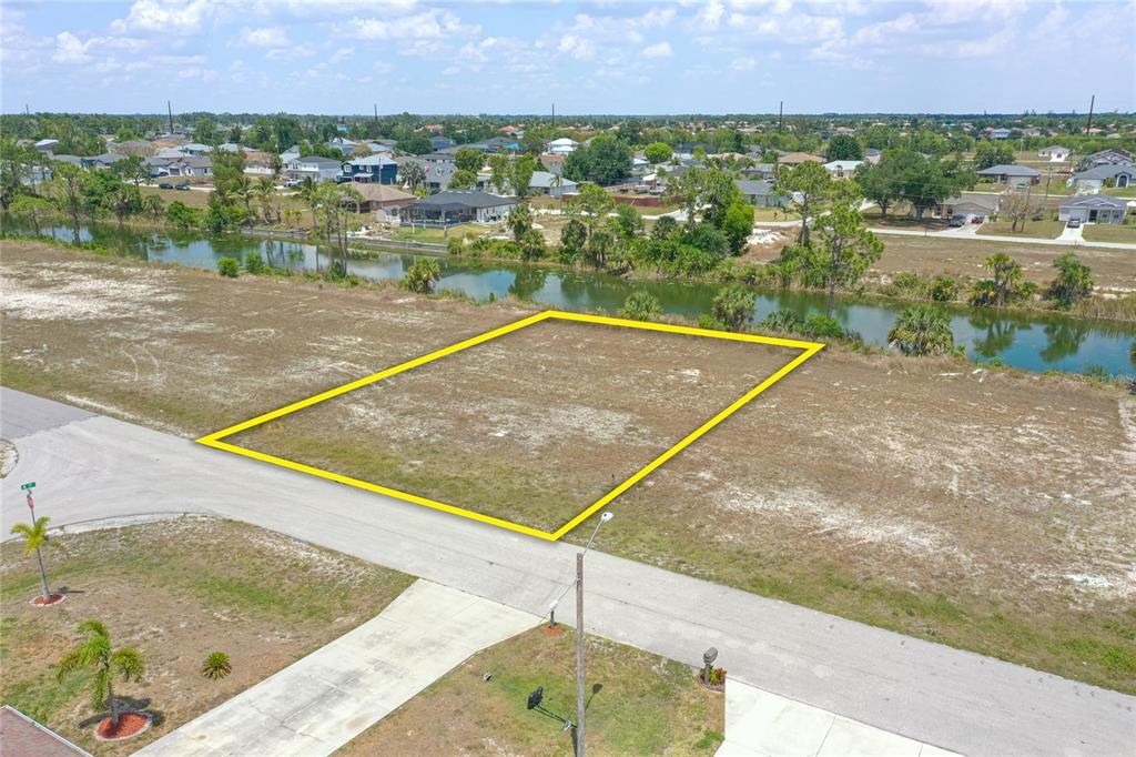 An aerial view shows a vacant, rectangular residential lot outlined in yellow bordering a canal — 2831 NE 5TH PLACE, CAPE CORAL, FL