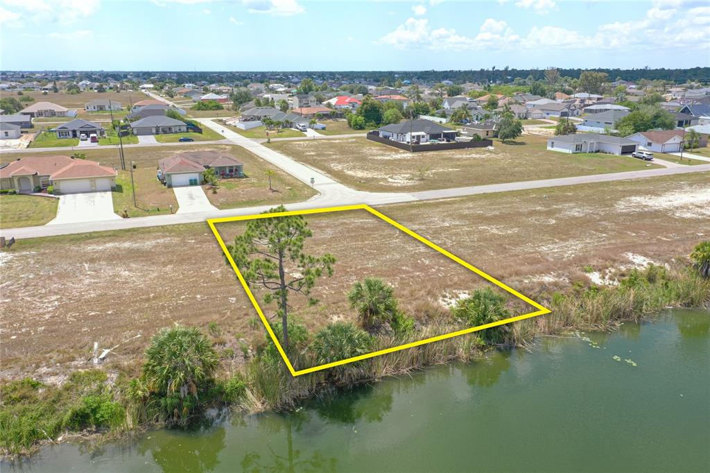 An aerial view shows a vacant waterfront lot outlined in yellow near residential houses — 2831 NE 5TH PLACE, CAPE CORAL, FL