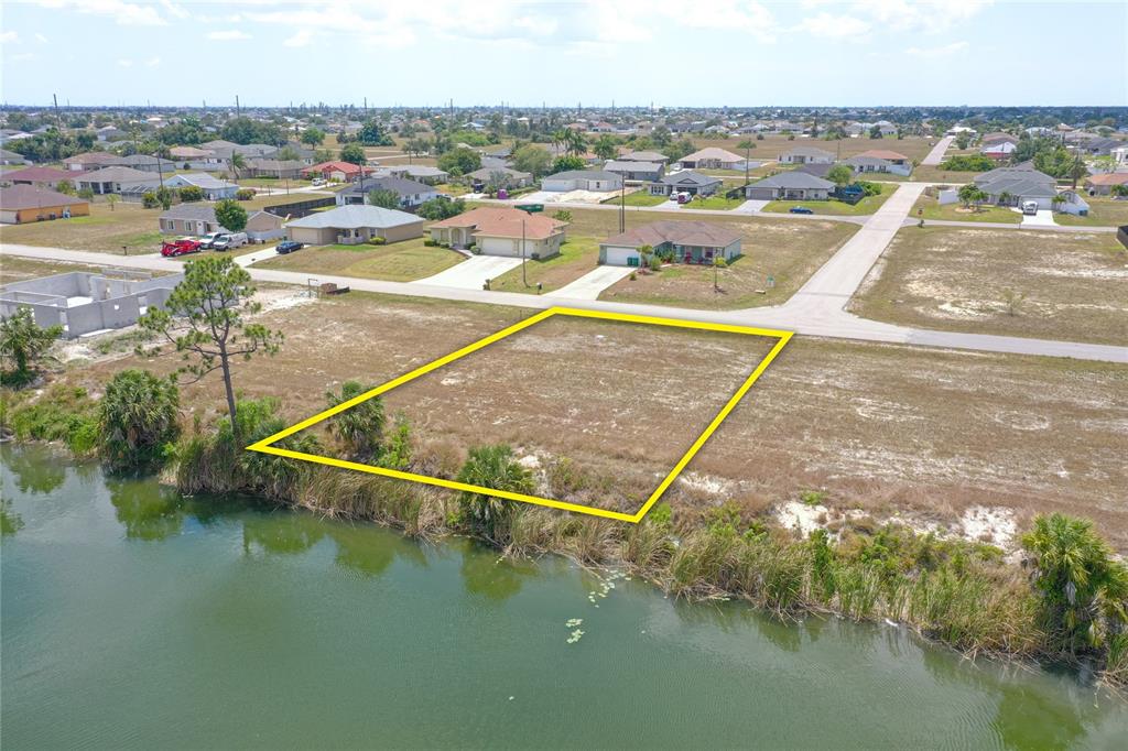 An aerial view shows a vacant, rectangular waterfront lot outlined in yellow near residential houses — 2831 NE 5TH PLACE, CAPE CORAL, FL