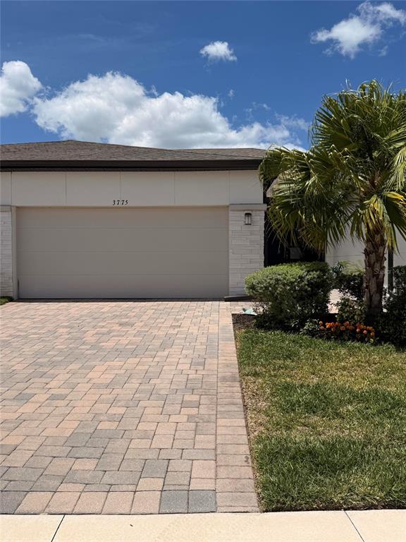 A paved driveway leads to a two-car garage with a light-colored exterior and palm tree — 3775 MAXWELL PARK DRIVE UNIT 3775, SUN CITY CENTER, FL