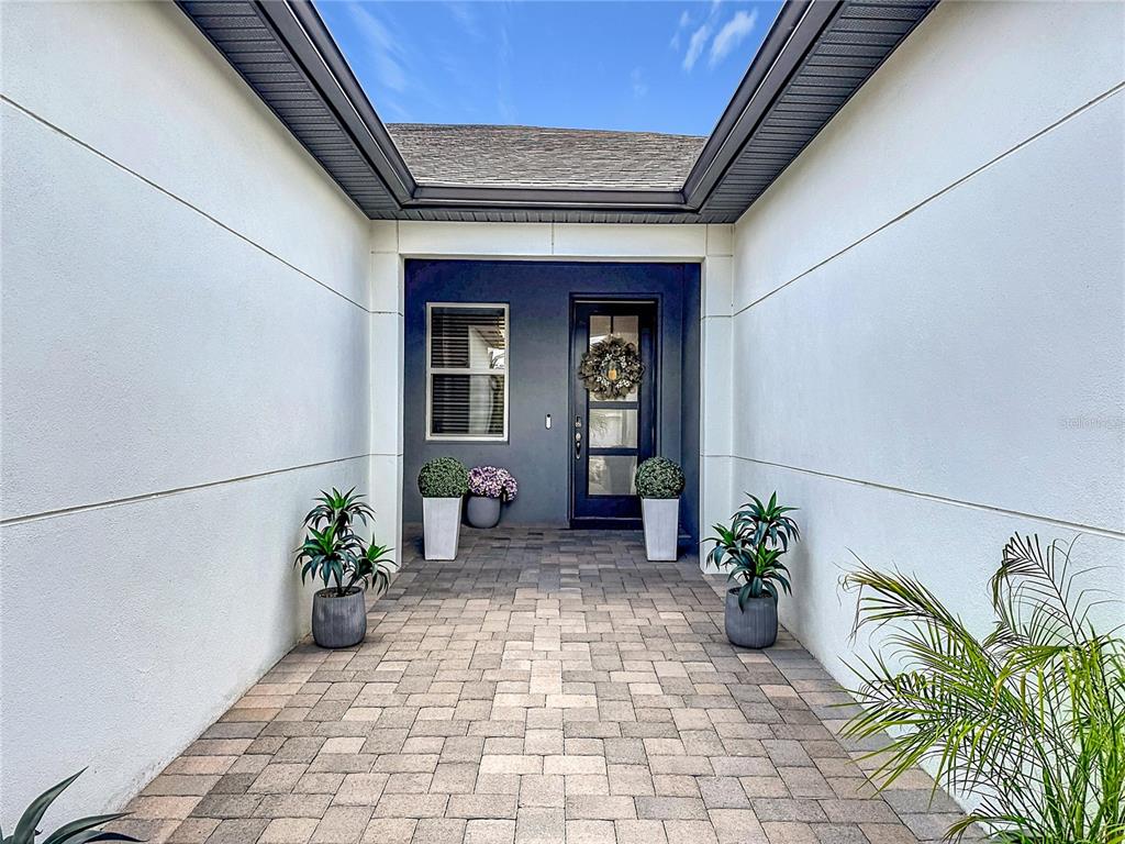 A paved entryway leads to a dark front door flanked by potted plants and windows — 3775 MAXWELL PARK DRIVE UNIT 3775, SUN CITY CENTER, FL