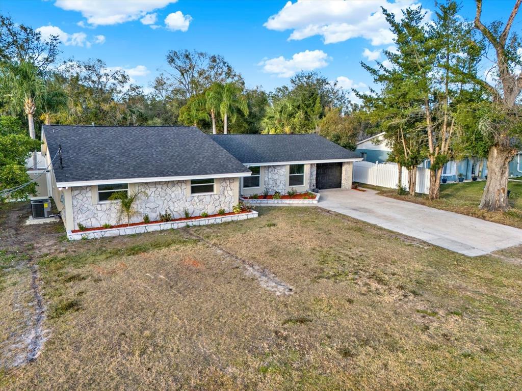 A single-story house with a stone facade, dark shingled roof, and a concrete driveway — 18803 TRACER DRIVE, LUTZ, FL