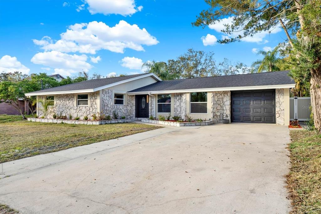 A single-story house with a stone facade, dark garage door, and a concrete driveway — 18803 TRACER DRIVE, LUTZ, FL