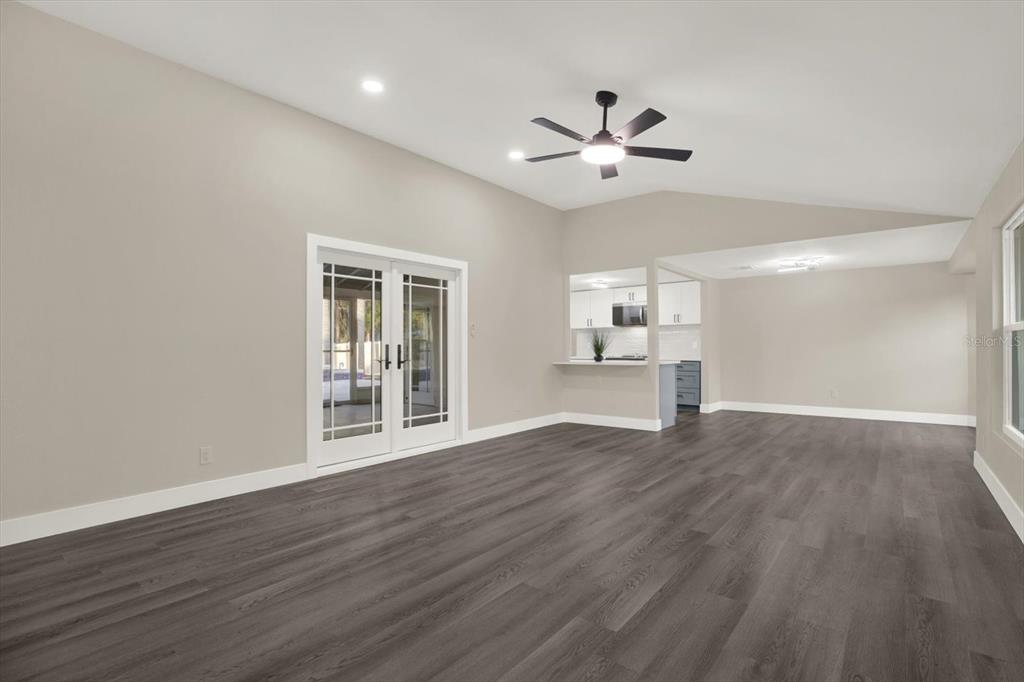 A living room with gray wood-look flooring, vaulted ceilings, and French doors leading outside — 18803 TRACER DRIVE, LUTZ, FL