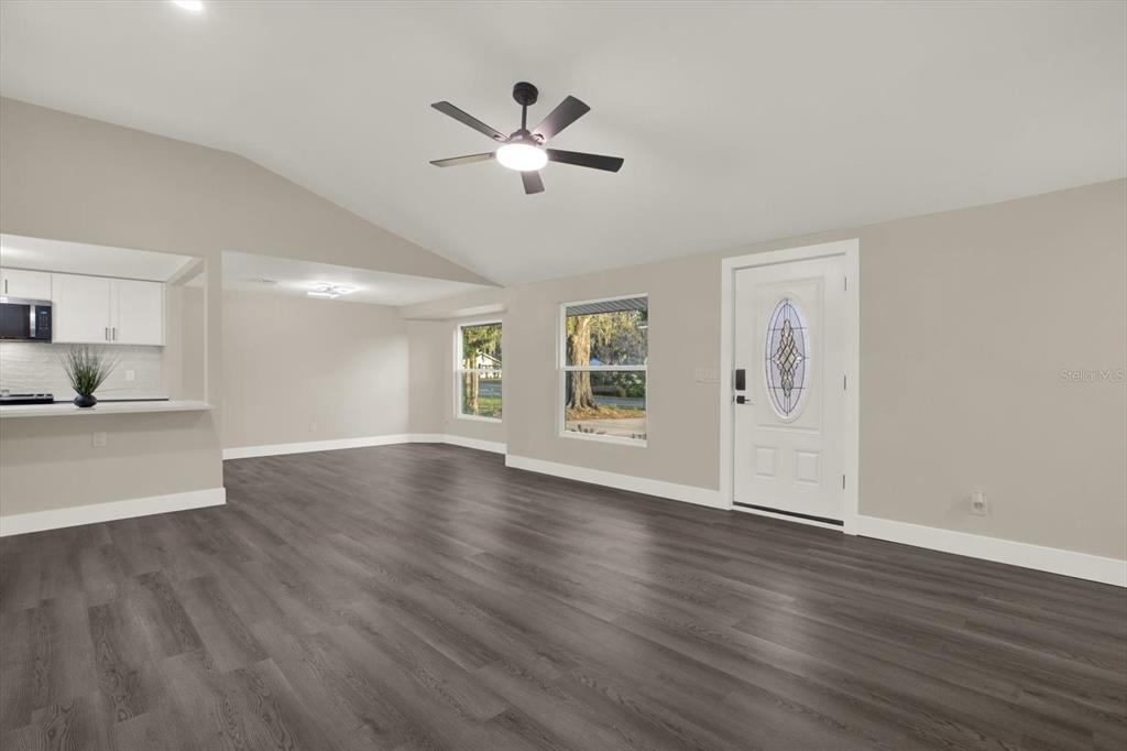 A living room with gray wood-look flooring, a vaulted ceiling, and a white front door — 18803 TRACER DRIVE, LUTZ, FL