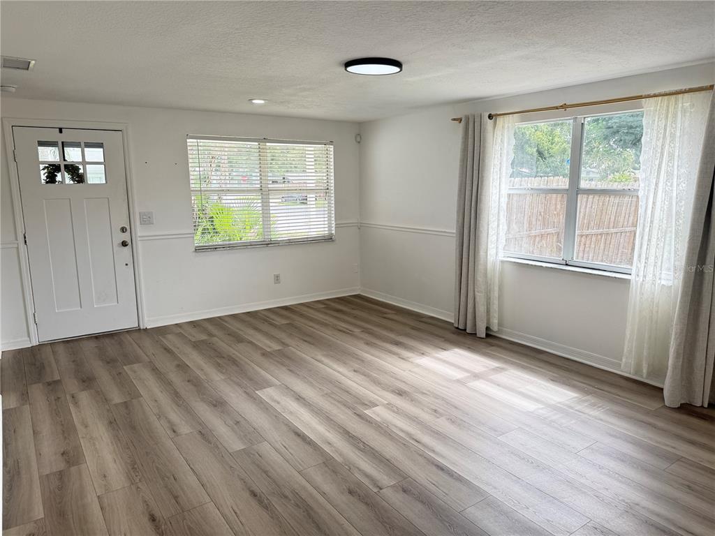 A living room features light wood-look flooring, white walls with chair rail molding, and two windows — 6150 101ST AVENUE N, PINELLAS PARK, FL