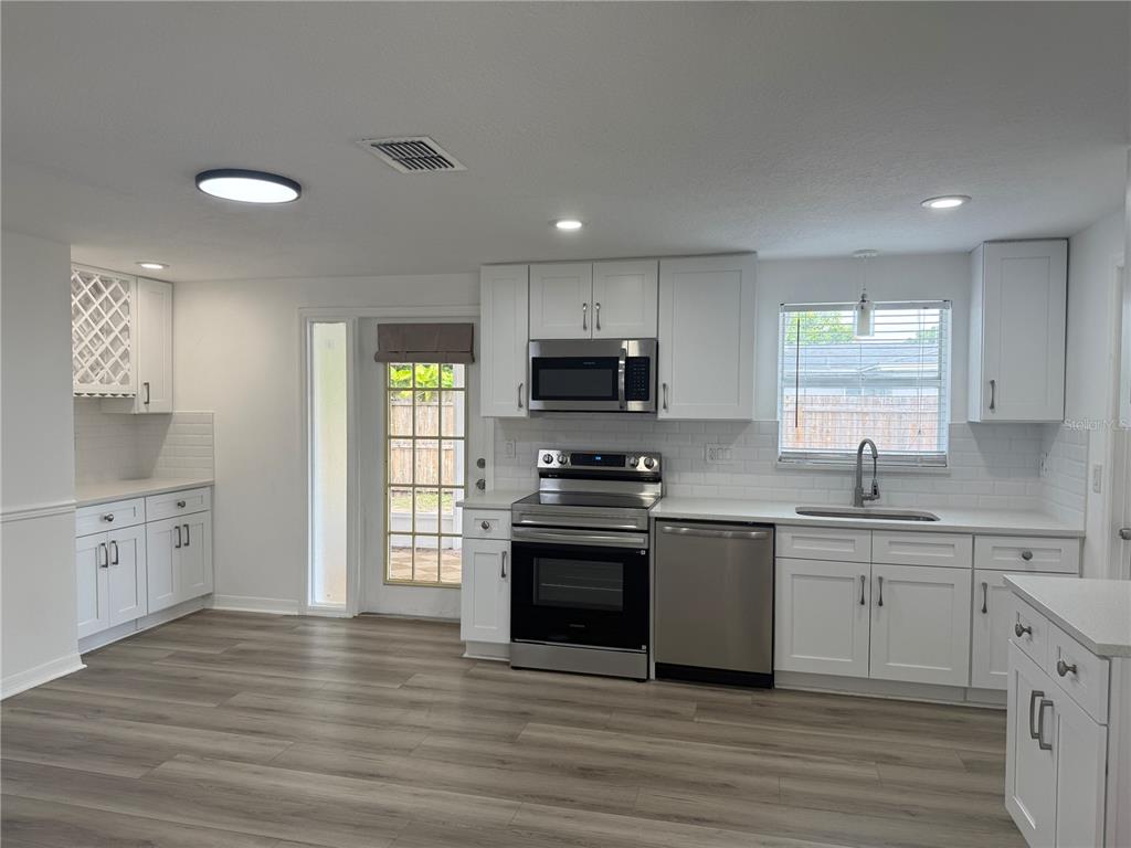 A bright kitchen features white cabinets, stainless steel appliances, subway tile backsplash, and wood-look flooring — 6150 101ST AVENUE N, PINELLAS PARK, FL