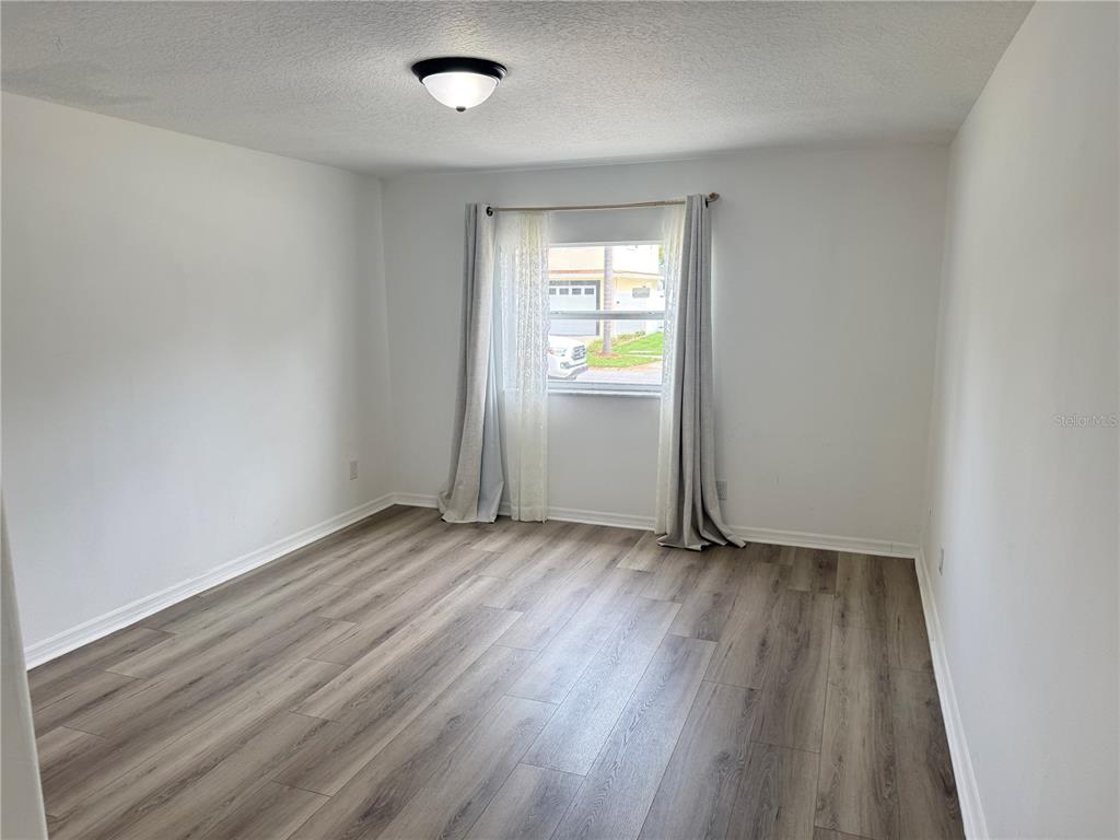 An empty bedroom features white walls, wood-look flooring, a ceiling light, and a window — 6150 101ST AVENUE N, PINELLAS PARK, FL
