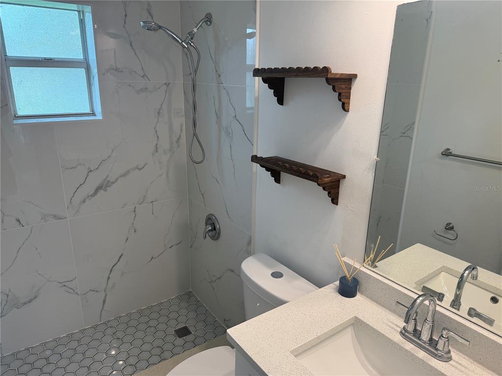 A bathroom features a marble-tiled walk-in shower, a white vanity, and two wooden wall shelves — 6150 101ST AVENUE N, PINELLAS PARK, FL