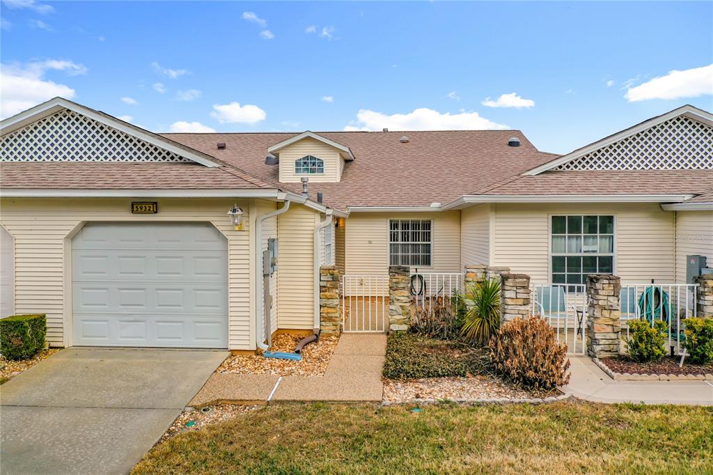 A single-story house with a garage, light siding, and a small gated courtyard entrance — 5932 MCENROE COURT, LEESBURG, FL