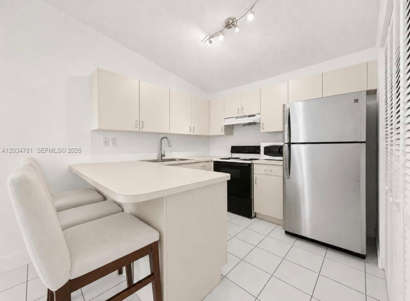 A kitchen with white cabinets, stainless steel appliances, a breakfast bar, and white tile flooring — 7611 SW 153rd Ct # 204, Miami FL 33193, MIAMI, FL