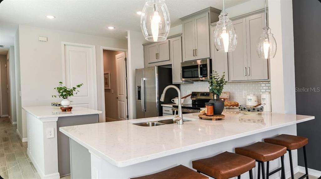 A kitchen features grey cabinets, white countertops, a central island, and three leather bar stools — 11751 SOFT MEADOW MEWS, SAN ANTONIO, FL