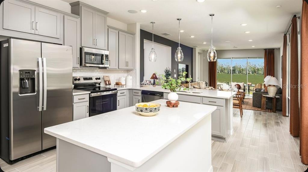 A modern kitchen with gray cabinets, stainless steel appliances, and a large white island — 11751 SOFT MEADOW MEWS, SAN ANTONIO, FL