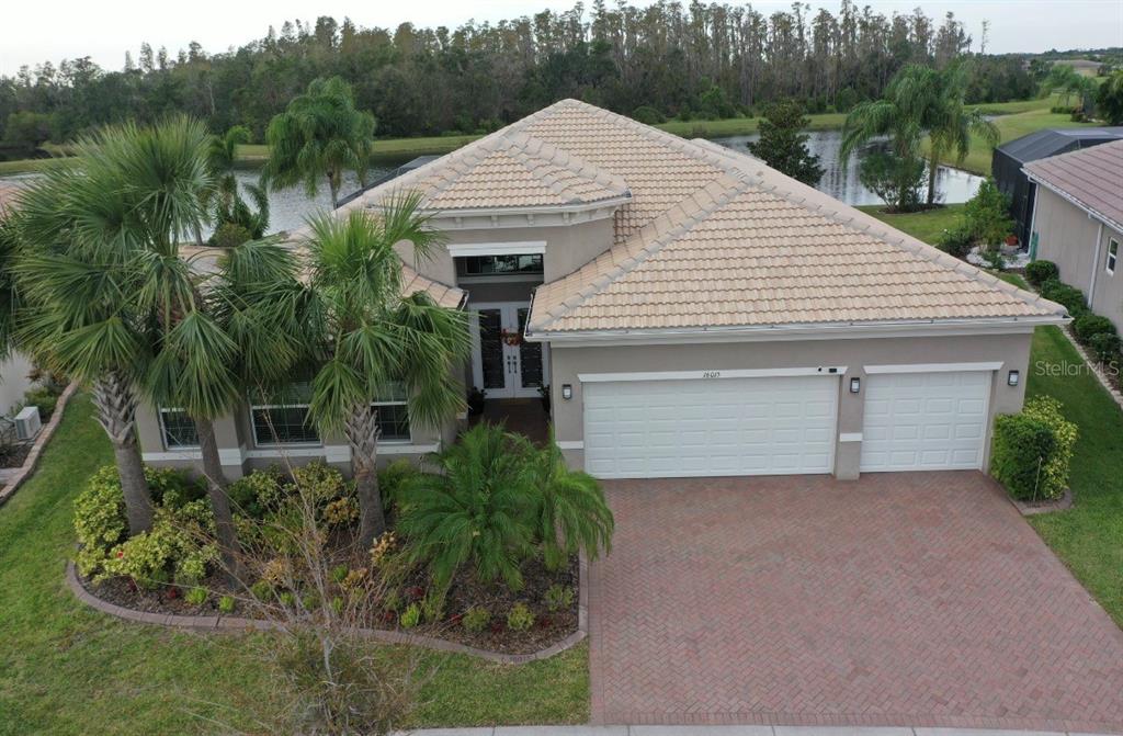A front entryway features double glass-paneled doors, a floral wreath, and two potted plants — 16015 CAPE CORAL DRIVE, WIMAUMA, FL