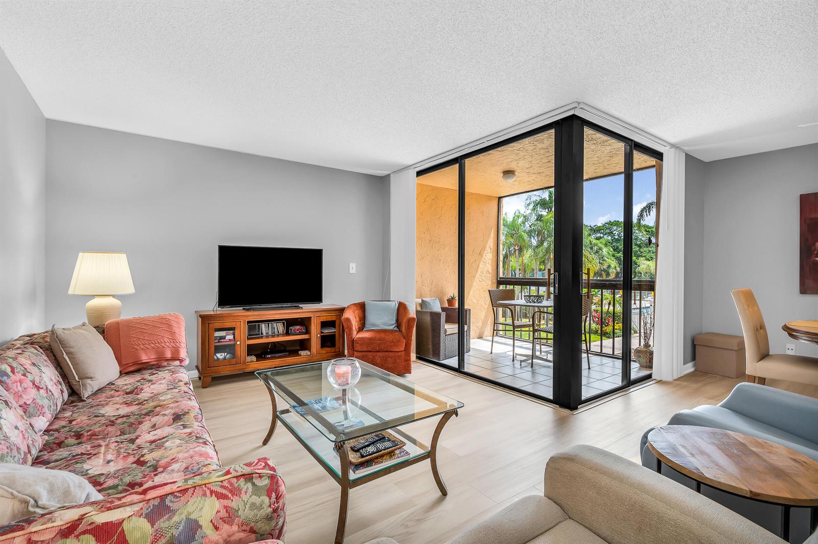 A living room features a floral sofa, glass coffee table, and sliding doors to a balcony — 2255 Lindell Boulevard # 4207, Delray Beach FL 33444, DELRAY BEACH, FL