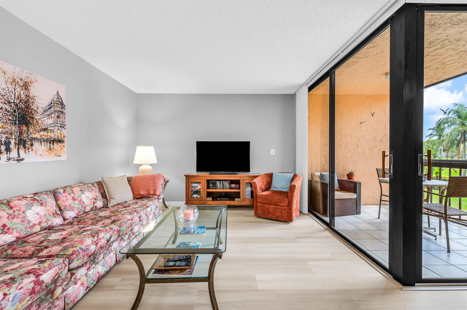 A living room features a floral sofa, glass coffee table, and sliding doors to a balcony — 2255 Lindell Boulevard # 4207, Delray Beach FL 33444, DELRAY BEACH, FL