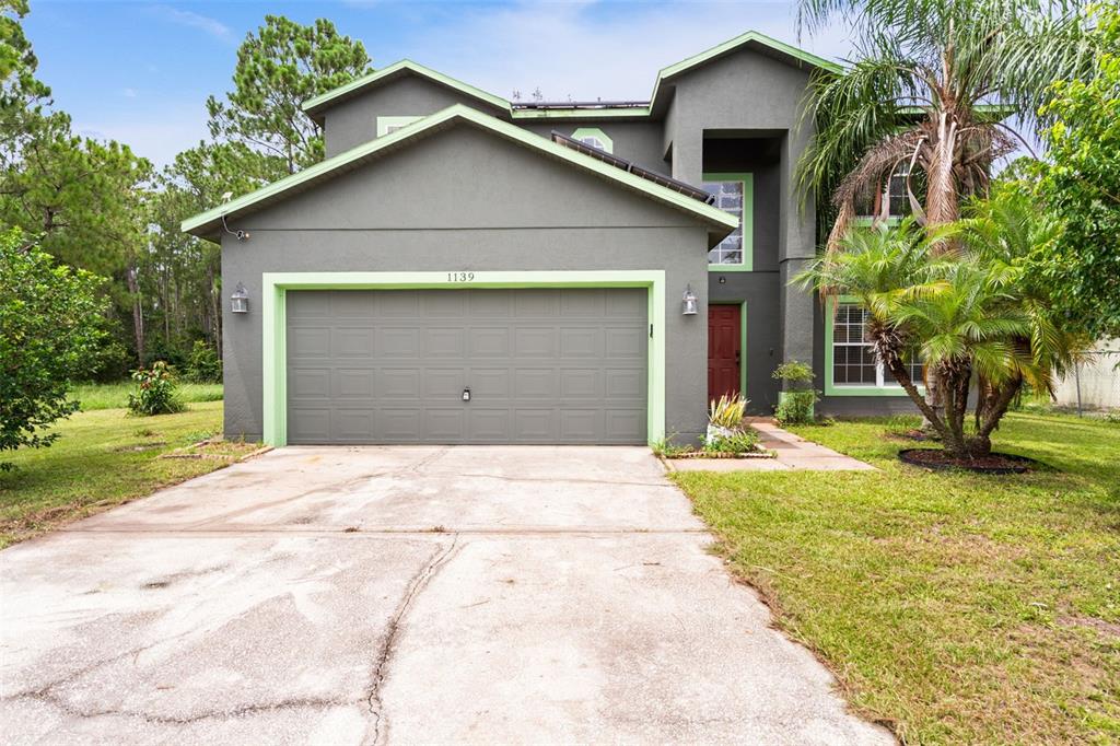 A two-story house with a gray stucco exterior, lime green trim, and a concrete driveway — 1139 CAMBOURNE DRIVE, KISSIMMEE, FL