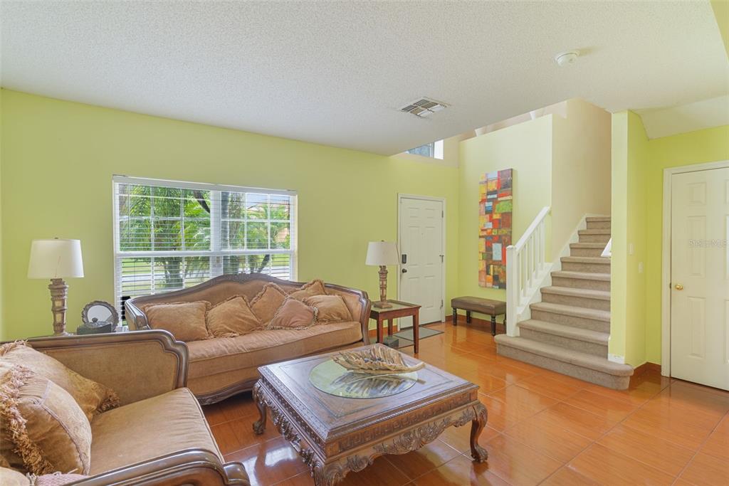 A living room features light green walls, tile flooring, a staircase, and traditional brown furniture — 1139 CAMBOURNE DRIVE, KISSIMMEE, FL