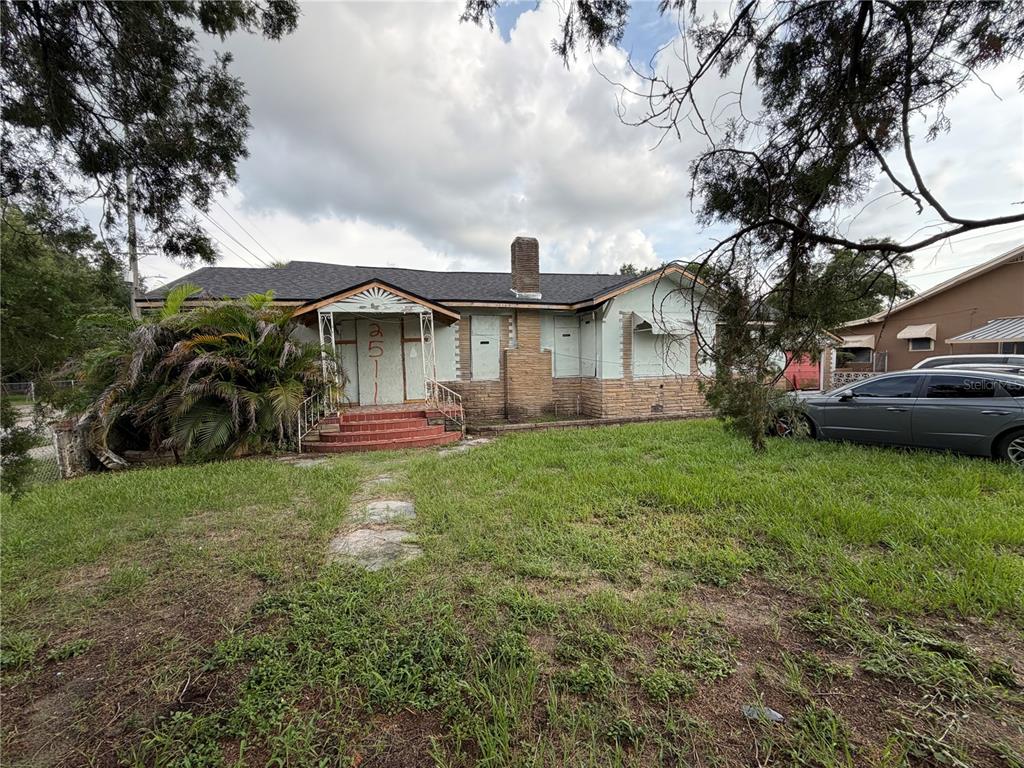 A single-story house with boarded-up windows and a stone chimney sits on a grassy lot — 2511 E 21ST AVENUE, TAMPA, FL