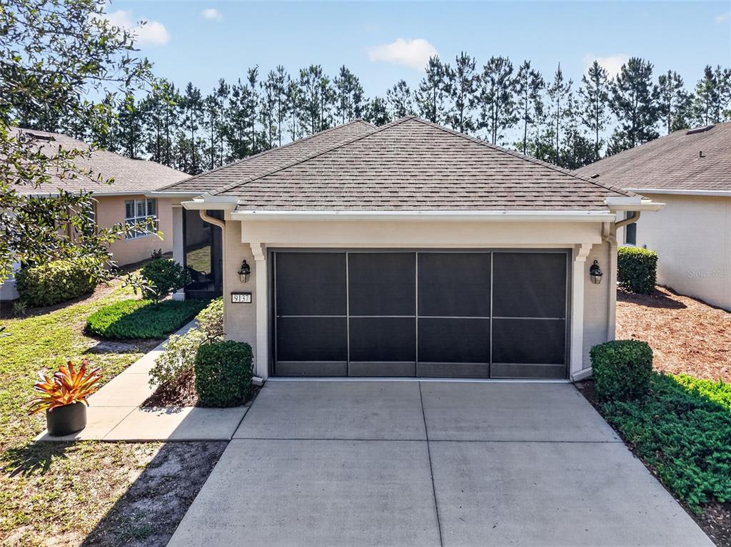 A single-story house exterior features a dark screen-covered garage door and a concrete driveway — 9137 SW 70TH LOOP, OCALA, FL