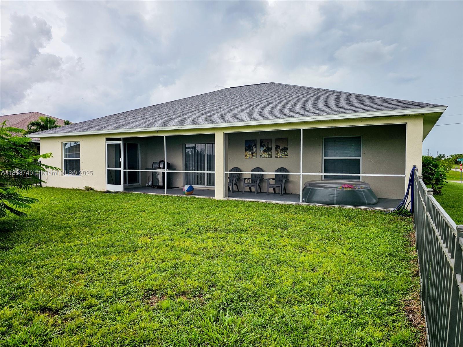 The exterior of a house features a screened-in patio overlooking a grassy backyard — 1000 NW 24TH AVE, Cape Coral FL 33993, CAPE CORAL, FL