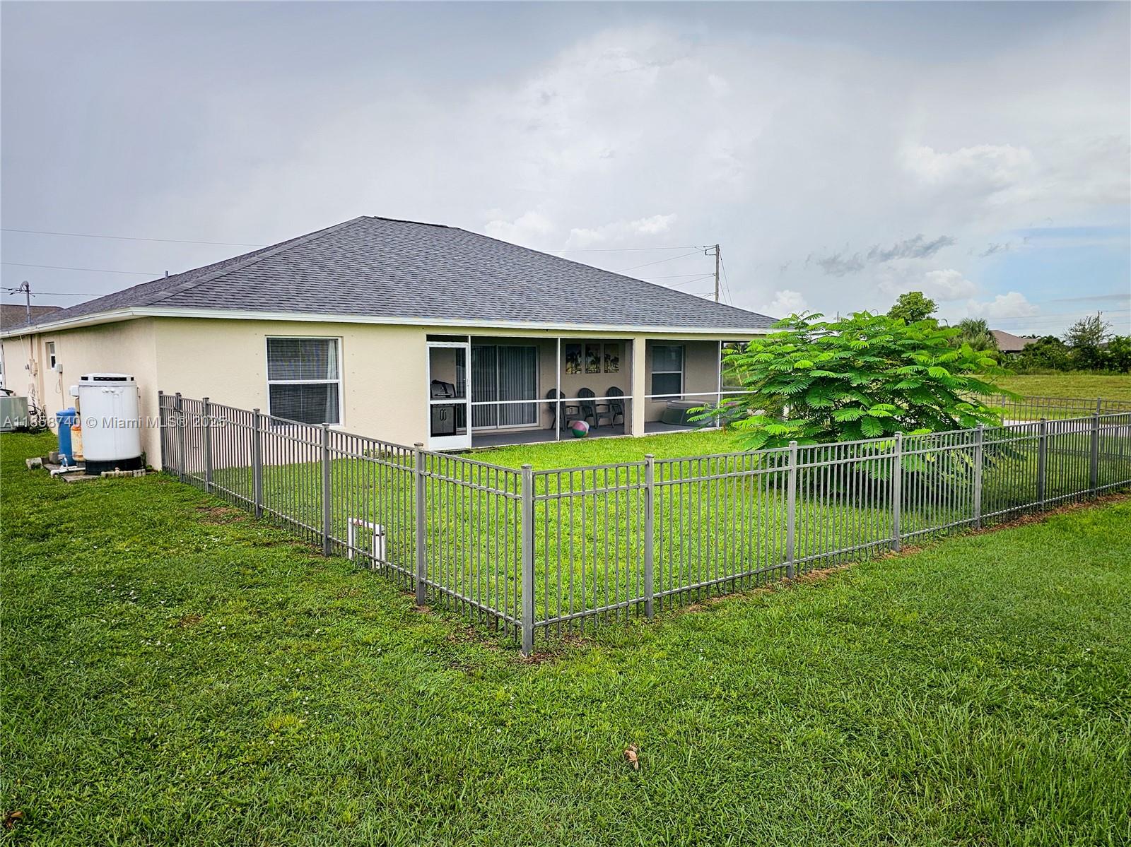 The backyard of a house features a screened-in patio and a metal fence — 1000 NW 24TH AVE, Cape Coral FL 33993, CAPE CORAL, FL